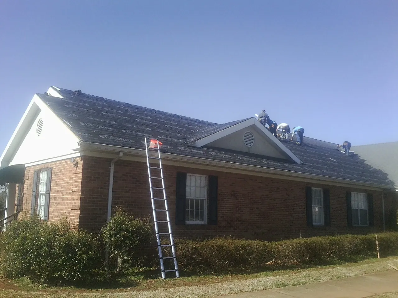 Crew tearing shingles off a brick ranch roof with a ladder set — Emergency Roof Repair work by our crew in Clinton Corners