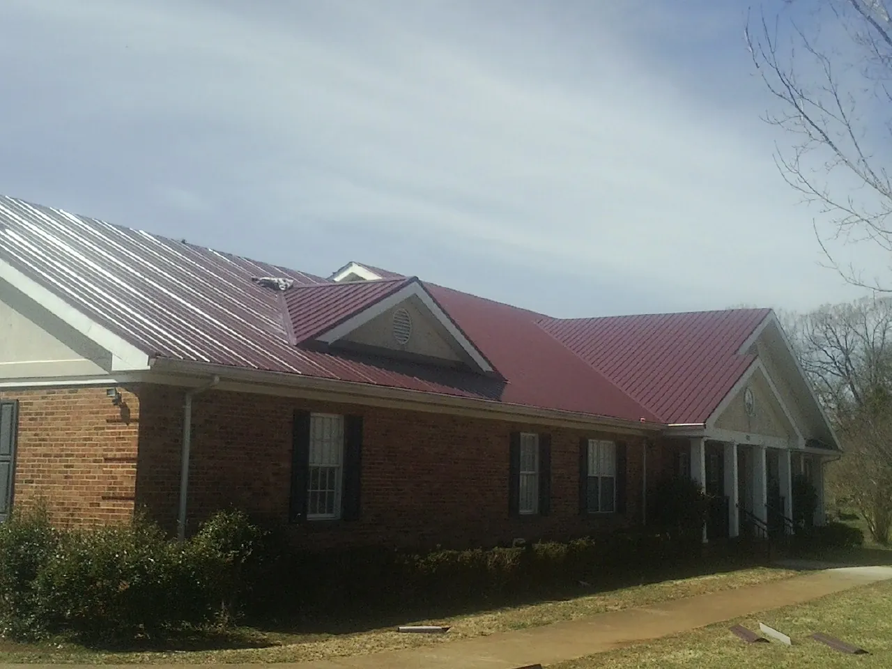 Red metal roof with gabled entries on a long brick building, from a Hail Damage Roof Repair job in Clinton Corners