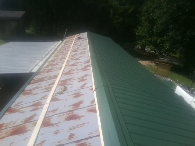 Old rusted panels beside newly installed green metal roofing — Wind Damage Roof Repair by Roofing Brothers in Clinton Corners