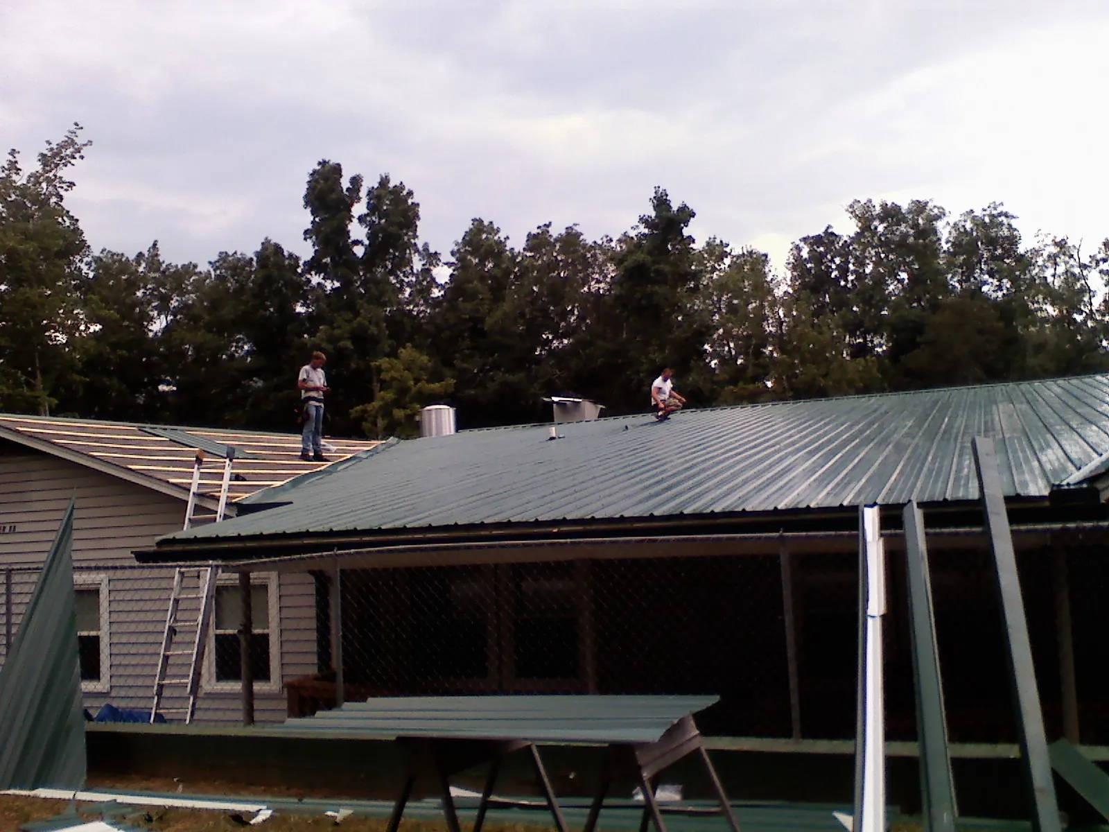 Two roofers installing green metal panels above a covered porch in Clinton Corners