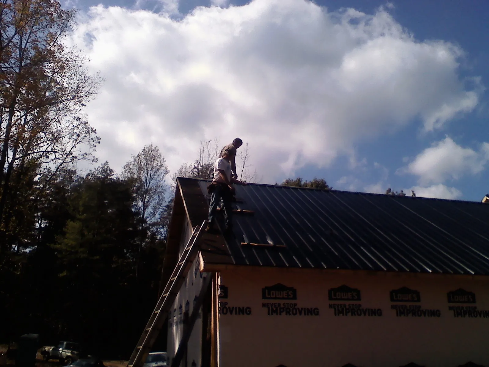 Roofer fastening dark metal panels high against a cloudy sky, from a Roof Inspection job in Clinton Corners