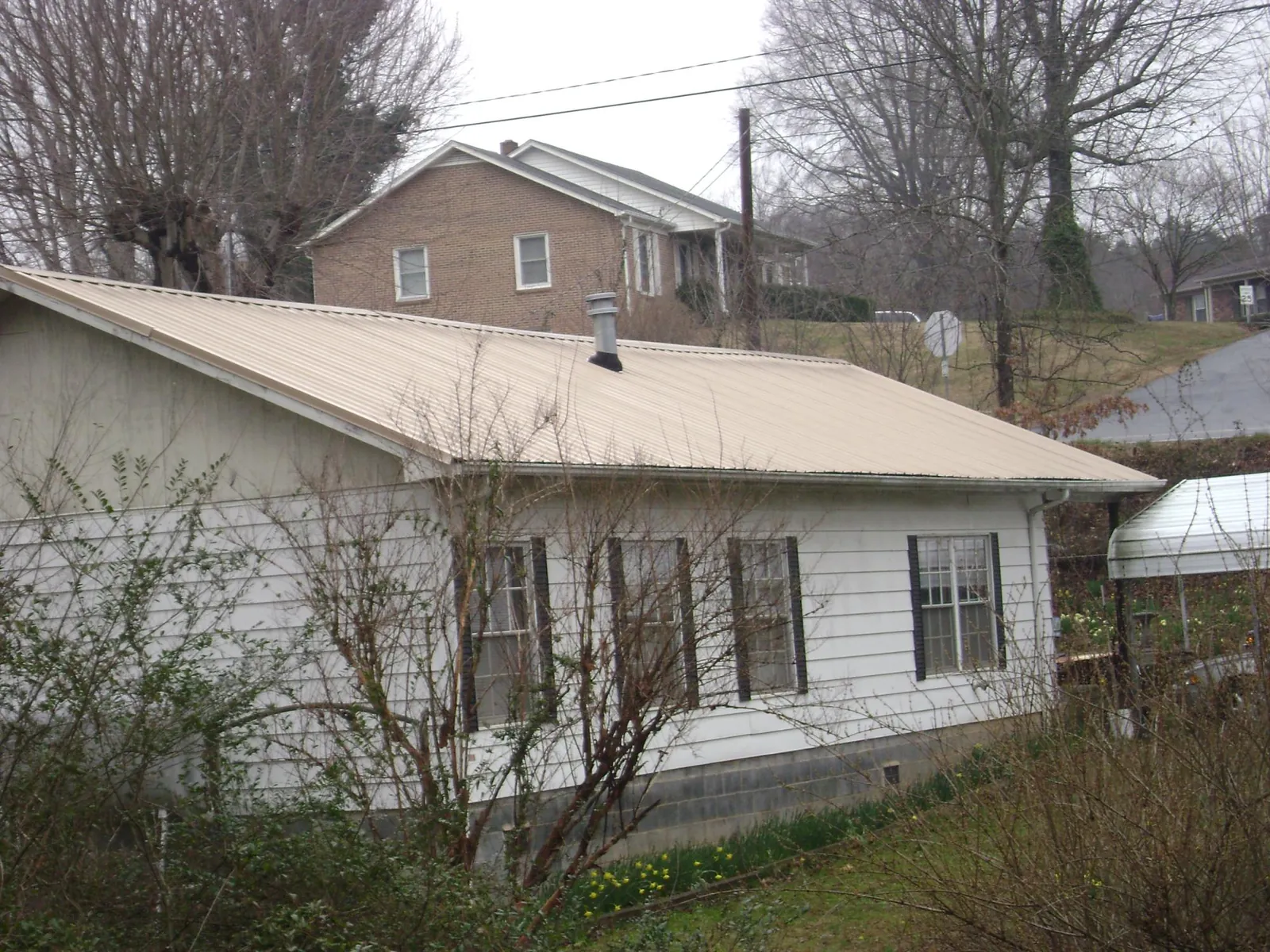 Tan metal roof on a white sided house set into a hillside — Commercial Roofing by Roofing Brothers in Clinton Corners